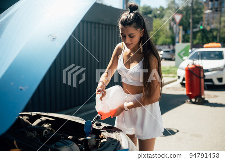 Young woman pouring antifreeze car screen wash liquid into car 94791458