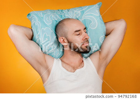 The concept of rest. Man, folding his hands under his pillow, sleeps overuses to the side. Orange background 94792168
