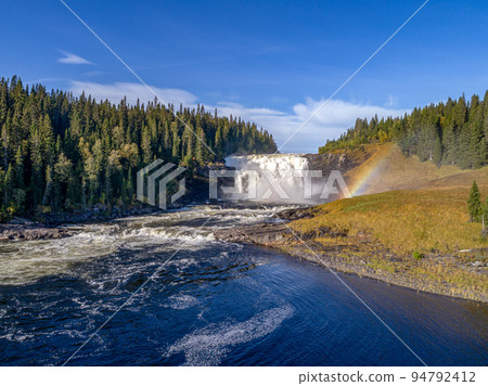 Aerial view famous waterfall Tannforsen northern Sweden, with a rainbow in the mist and rapid flowing cascades of water Aerial view famous waterfall Tannforsen northern Sweden, with a rainbow in the mist and rapid flowing cascades of water 94792412