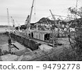 A group of cranes in an industrial area by the sea 94792778