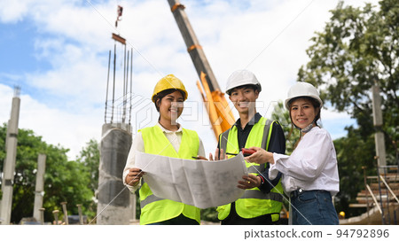 Civil engineer team in safety helmet standing at the construction site with crane and beautiful sky in background Civil engineer team in safety helmet standing at the construction site with crane and beautiful sky in background 94792896