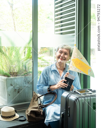 60 歲亞洲老婦老婦人像,微笑,坐著,拿著手提箱,拿著旗桿,製作旅行團概念。 60 歲亞洲老婦老婦人像,微笑,坐著,拿著手提箱,拿著旗桿,製作旅行團概念。 94793272