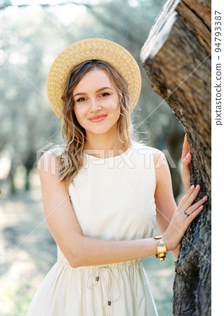 Girl in a straw hat stands near a tree in an olive grove. Portrait Girl in a straw hat stands near a tree in an olive grove. Portrait 94793387