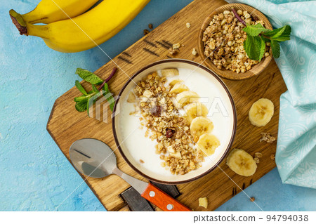 Granola. Granola with yogurt, chocolate and banana on blue concrete or stone table. The concept of healthy nutrition and diet. Top view flat lay background. Granola. Granola with yogurt, chocolate and banana on blue concrete or stone table. The concept of healthy nutrition and diet. Top view flat lay background. 94794038