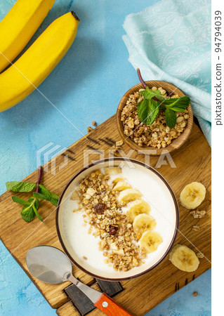 Granola. Granola with yogurt, chocolate and banana on blue concrete or stone table. The concept of healthy nutrition and diet. Top view flat lay background. Granola. Granola with yogurt, chocolate and banana on blue concrete or stone table. The concept of healthy nutrition and diet. Top view flat lay background. 94794039