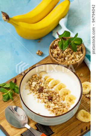 Granola. Granola with yogurt, chocolate and banana on blue concrete or stone table. The concept of healthy nutrition and diet. Copy space. Granola. Granola with yogurt, chocolate and banana on blue concrete or stone table. The concept of healthy nutrition and diet. Copy space. 94794042