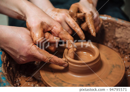 Potter teach pupil on circle wheel in workshop. Hands Close up Potter teach pupil on circle wheel in workshop. Hands Close up 94795571