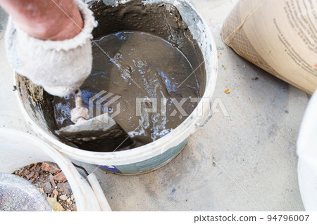 a gloved man's hand kneads cement mortar with a trowel. a gloved man's hand kneads cement mortar with a trowel. 94796007