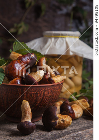 Pile of Imleria Badia or Boletus badius mushrooms commonly known as the bay bolete with canned mushroom in glass jar on vintage wooden background.. Pile of Imleria Badia or Boletus badius mushrooms commonly known as the bay bolete with canned mushroom in glass jar on vintage wooden background.. 94798108