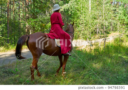 Woman in red dress rides a horse in early spring 94798391