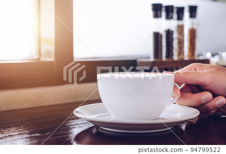 Cropped shot view of a cup of coffee with women hand. 94799522
