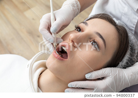 Young woman having dental check up in dental clinic. Dentist examining a patient teeth with dental mirror 94800337