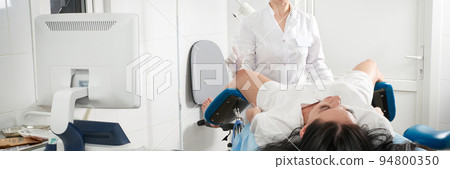 Cropped panorama of gynecologist examining a patient who is sitting in a gynecological chair. Female health concept. 94800350