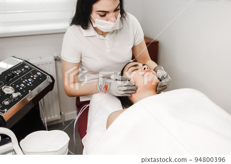Microcurrent therapy. Cosmelotologist makes stimulating facial massage with electric gloves. Lymphatic drainage massage 94800396