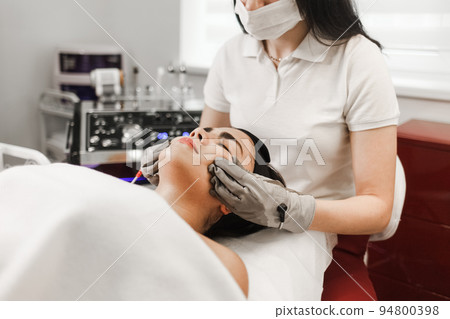 Microcurrent therapy. Cosmelotologist makes stimulating facial massage with electric gloves. Lymphatic drainage massage.. Microcurrent therapy. Cosmelotologist makes stimulating facial massage with electric gloves. Lymphatic drainage massage.. 94800398