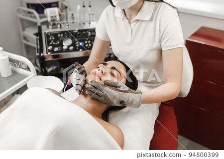 Microcurrent therapy. Cosmelotologist makes stimulating facial massage with electric gloves. Lymphatic drainage massage.. Microcurrent therapy. Cosmelotologist makes stimulating facial massage with electric gloves. Lymphatic drainage massage.. 94800399