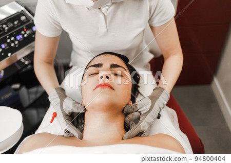 Microcurrent therapy. Cosmelotologist makes stimulating facial massage with electric gloves. Lymphatic drainage massage Microcurrent therapy. Cosmelotologist makes stimulating facial massage with electric gloves. Lymphatic drainage massage 94800404
