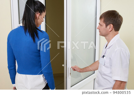 Doctor opens a door to his office and invites patient to enter Doctor opens a door to his office and invites patient to enter 94800535