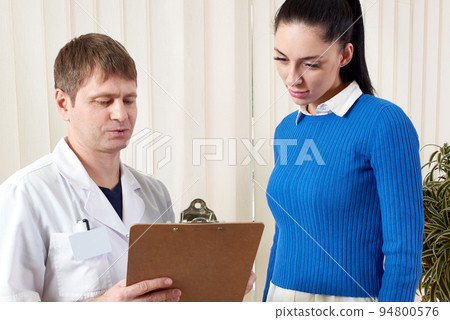 Doctor showing female patient her medical test results in corridor Doctor showing female patient her medical test results in corridor 94800576