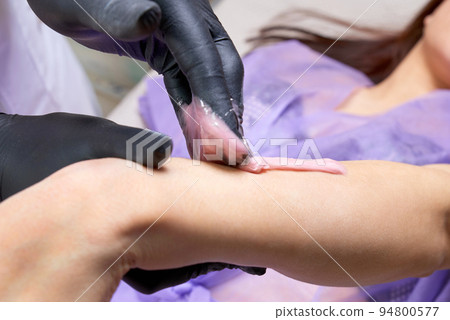 Process of waxing in a beauty salon by a professional beautician. Beauty salon worker applying wax and tape to remove hair from arms Process of waxing in a beauty salon by a professional beautician. Beauty salon worker applying wax and tape to remove hair from arms 94800577
