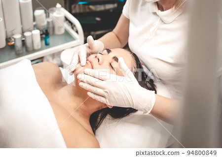 Cosmetologist massages the client's face. Cosmetologist massages the client's face. 94800849
