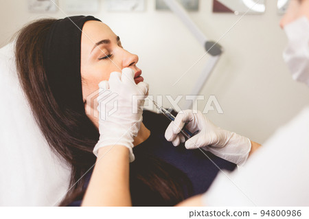 Woman fights facial wrinkles. Doctor cosmetologist gives a chin injection for patient.. 94800986