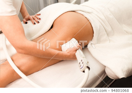 Doctor cosmetologist with a roller in his hands makes a buttocks massage with device closeup.. Doctor cosmetologist with a roller in his hands makes a buttocks massage with device closeup.. 94801068