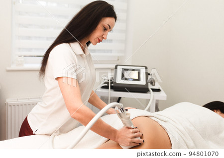 Doctor cosmetologist with a roller in his hands makes a buttocks massage with device.. Doctor cosmetologist with a roller in his hands makes a buttocks massage with device.. 94801070