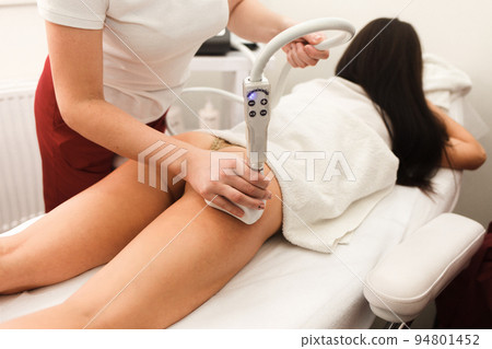 Doctor cosmetologist with a roller in his hands makes a buttocks massage with device. Doctor cosmetologist with a roller in his hands makes a buttocks massage with device. 94801452