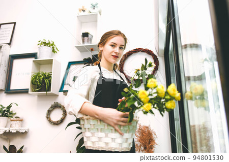 Young woman florist in a flower salon. Portrait of flower seller who holding a basket with roses. Young woman florist in a flower salon. Portrait of flower seller who holding a basket with roses. 94801530