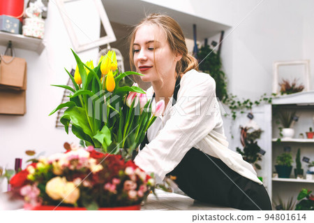 Flower shop seller sniffs tulips. Florist in flower market. 94801614