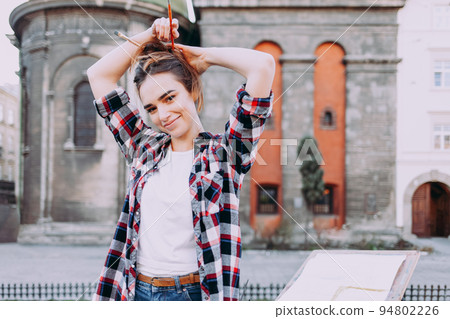 Young attractive girl braided brushes for drawing in her hair. Portrait of a cute painter artist. Young attractive girl braided brushes for drawing in her hair. Portrait of a cute painter artist. 94802226