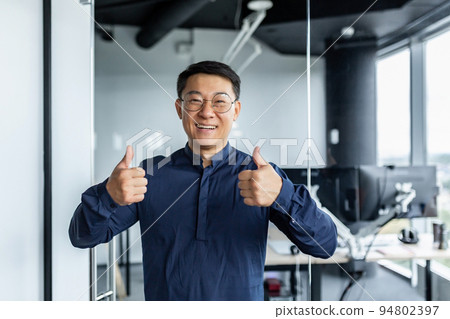 Portrait of successful asian businessman, man working in modern office looking at camera and smiling, broker trader showing thumbs up. 94802397