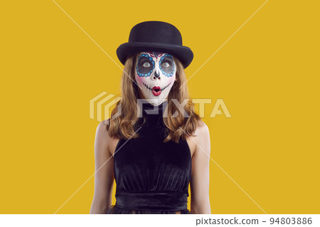 Wondering amazed woman in black halloween costume and hat with scary makeup on yellow background. 94803886