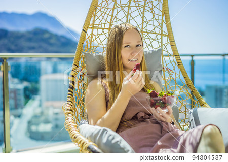 Portrait of gorgeous woman wearing beautiful dress sitting in a patio and eating strawberry Portrait of gorgeous woman wearing beautiful dress sitting in a patio and eating strawberry 94804587