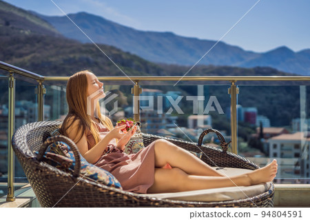 Portrait of gorgeous woman wearing beautiful dress sitting in a patio and eating strawberry Portrait of gorgeous woman wearing beautiful dress sitting in a patio and eating strawberry 94804591