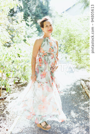 Beautiful happy mixed race Japanese woman in romantic floral maxi dress in summer park, smiling. Full body shot. Sunlight, copy space 94805613