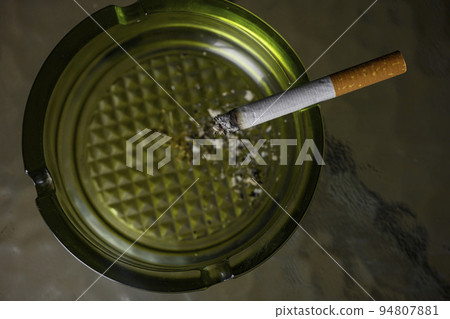Lit cigarette burning in ashtray close up 94807881