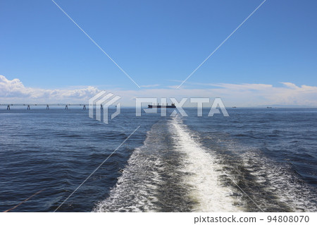 藍色海面海景與藍天、雲彩、陸上朦朧的島嶼和山脈、油輪、大型船隻、機場入口燈和船隻的白色尾波 94808070