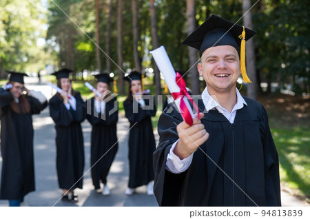 Happy young caucasian man celebrating graduation. Crowd of students graduates outdoors. 94813839