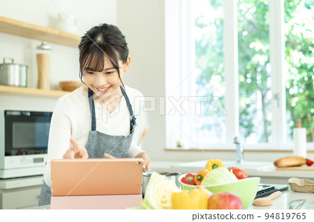 A young woman wearing an apron cooking while looking at a recipe 94819765