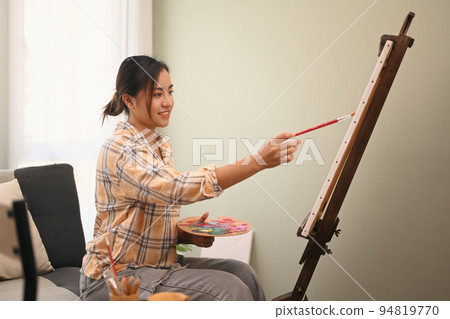Satisfied female painter painting on easel with watercolor in comfortable workshop. Leisure activity, creative hobby and art concept 94819770