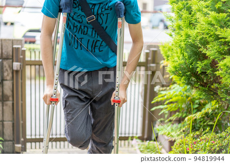 Man walking with crutches at the front door 94819944