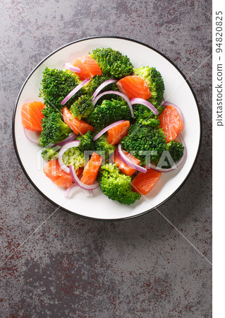 Dietary salad of steamed broccoli, salted salmon and red onion close-up in a plate. Vertical top view Dietary salad of steamed broccoli, salted salmon and red onion close-up in a plate. Vertical top view 94820825