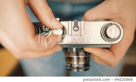 A young photographer changes shutter speed of a vintage old film camera and takes a picture. A young photographer changes shutter speed of a vintage old film camera and takes a picture. 94820866