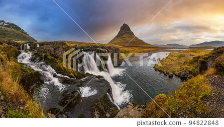 Famous picturesque Kirkjufell mountain and Kirkjufellsfoss waterfall next to Grundarfjordur at West Iceland autumn dusk view. 94822848