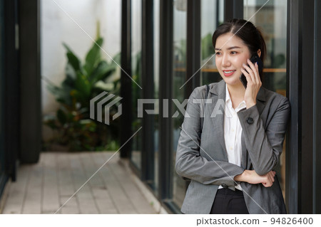 Young asian business woman smiling and talking on mobile phone, standing outside building Young asian business woman smiling and talking on mobile phone, standing outside building 94826400