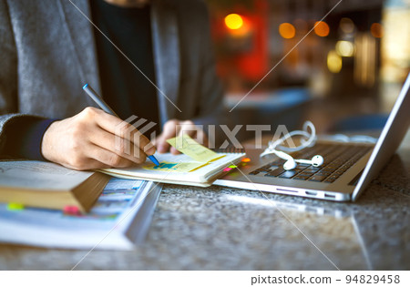 Shot of young male student sitting at table and writing on notebook. Male student studying in cafe. 94829458