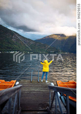 Girl tourist in a yellow jacket posing on the lake in Norway. Travelling, lifestyle, adventure. Girl tourist in a yellow jacket posing on the lake in Norway. Travelling, lifestyle, adventure. 94829858
