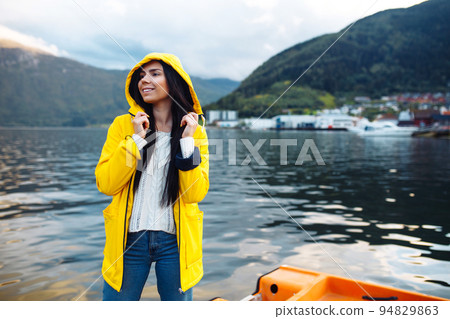 Girl tourist in yellow jacket posing on the lake in Norway. Active woman relaxing in the Norway. 94829863